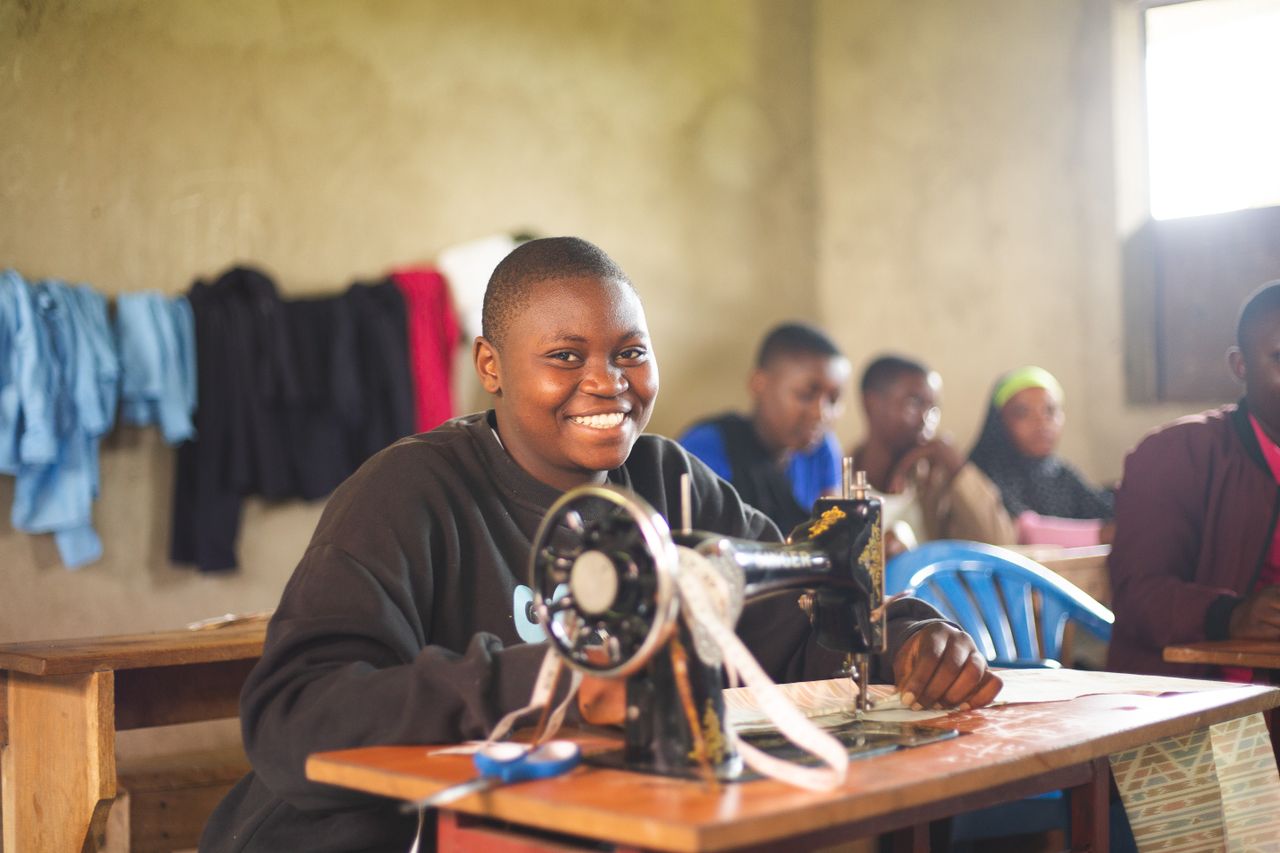 Happy student in Uganda using sewing machine in class, highlighting education.