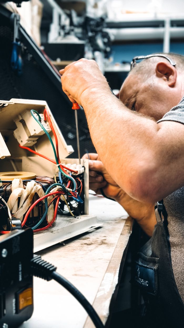 About Expert electrician repairing an electrical device in a workshop setting, focusing on wiring.